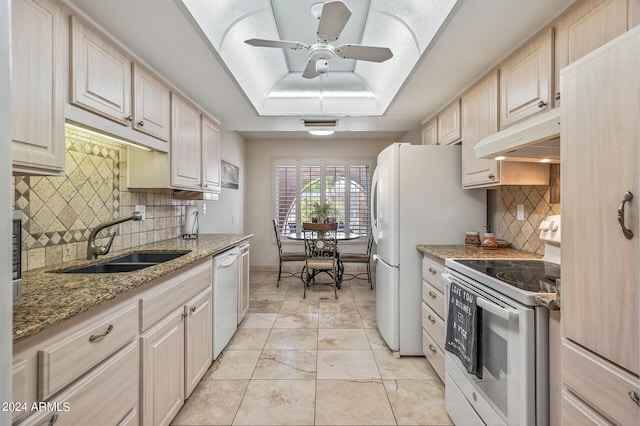 kitchen with a tray ceiling, a sink, light stone countertops, white appliances, and under cabinet range hood