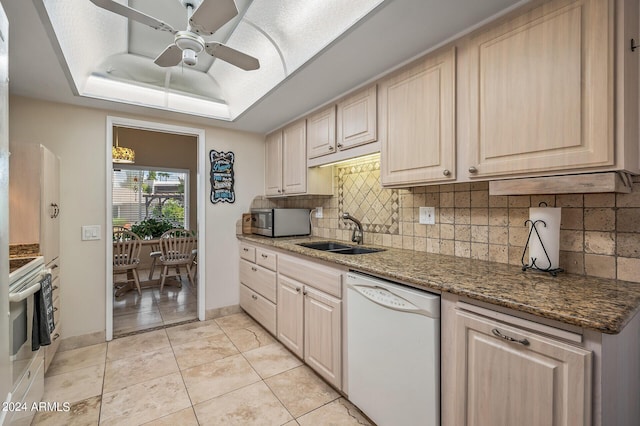 kitchen featuring white appliances, decorative backsplash, a raised ceiling, dark stone countertops, and a sink