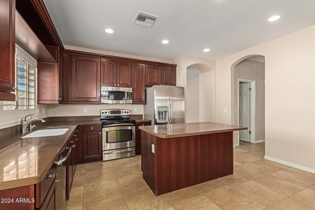 kitchen with light tile patterned flooring, appliances with stainless steel finishes, a center island, and sink