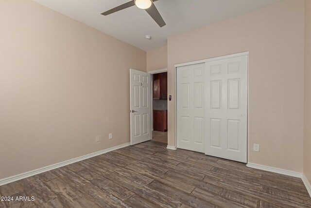 unfurnished bedroom with ceiling fan, a closet, and dark wood-type flooring