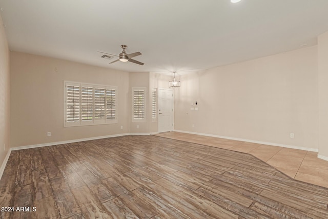 unfurnished room featuring ceiling fan with notable chandelier and light hardwood / wood-style flooring