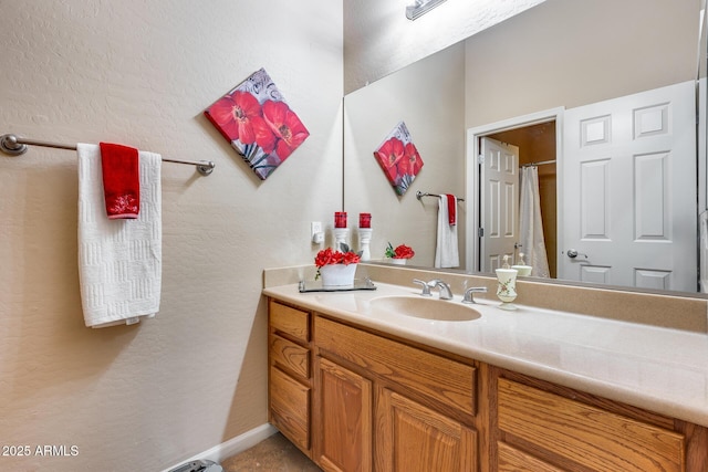 full bath featuring a shower with curtain, a textured wall, vanity, and baseboards