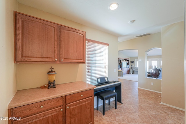 interior space featuring arched walkways, visible vents, baseboards, light countertops, and brown cabinets