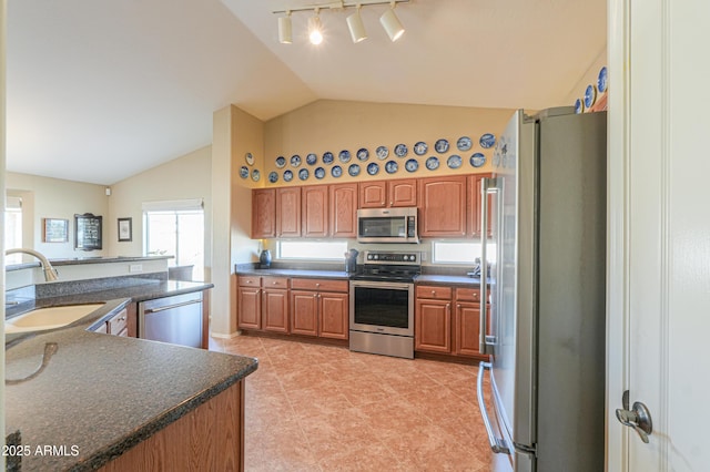 kitchen featuring a sink, vaulted ceiling, appliances with stainless steel finishes, brown cabinets, and dark countertops