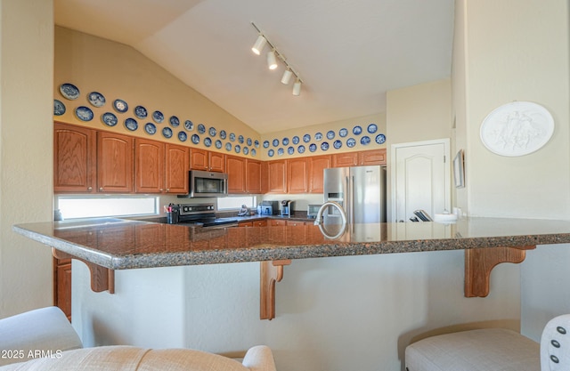 kitchen with stainless steel appliances, a peninsula, brown cabinets, dark countertops, and a kitchen bar