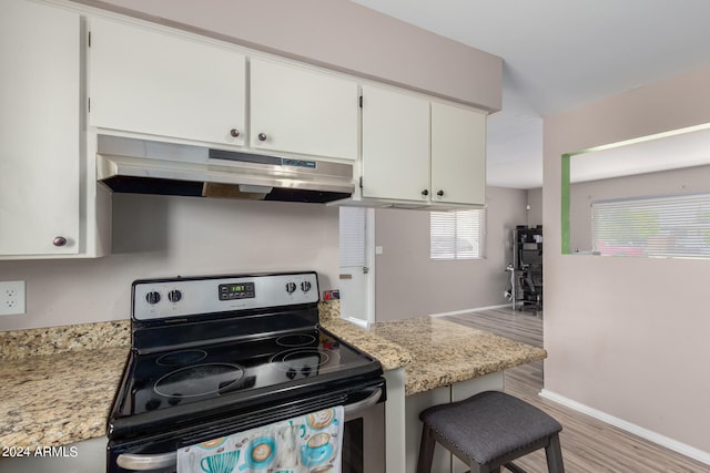 kitchen with a breakfast bar area, white cabinets, stainless steel electric range, light stone counters, and light hardwood / wood-style floors