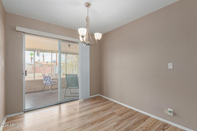 unfurnished room featuring an inviting chandelier and light wood-type flooring