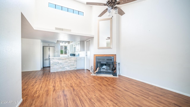 unfurnished living room with hardwood / wood-style floors, ceiling fan, sink, and a high ceiling