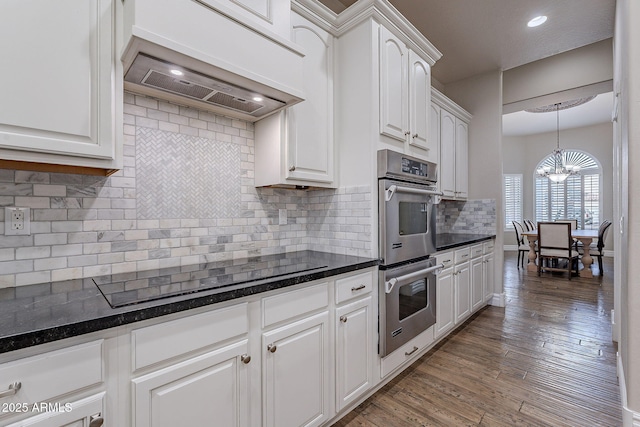 kitchen featuring premium range hood, an inviting chandelier, white cabinets, black electric stovetop, and stainless steel double oven