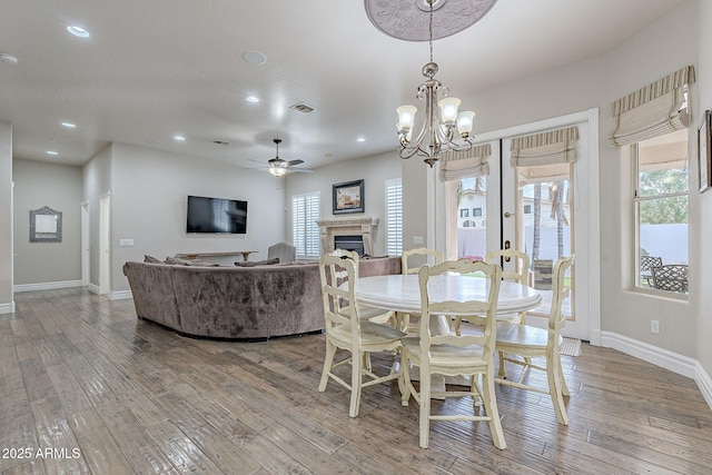 dining area with ceiling fan with notable chandelier, light wood-type flooring, and a wealth of natural light