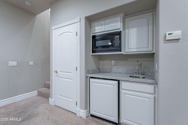 kitchen featuring black microwave, sink, white cabinets, and light carpet