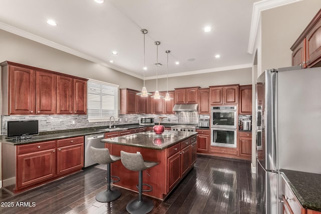 kitchen featuring dark wood finished floors, a sink, decorative backsplash, appliances with stainless steel finishes, and a center island