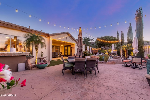 patio terrace at dusk featuring outdoor dining area and fence