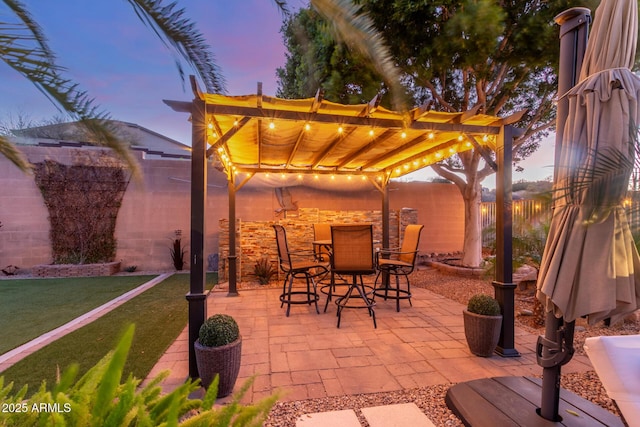 patio terrace at dusk featuring fence, outdoor dining space, a lawn, and a pergola