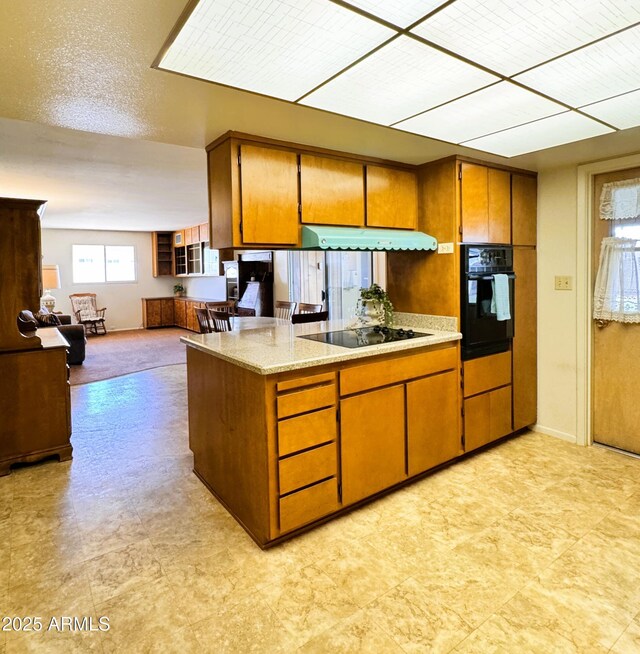 kitchen featuring brown cabinets, open floor plan, under cabinet range hood, and black appliances
