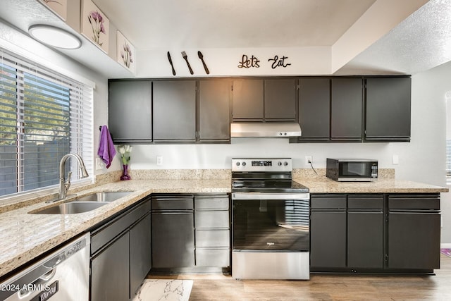 kitchen featuring sink, light wood-type flooring, a textured ceiling, light stone counters, and stainless steel appliances