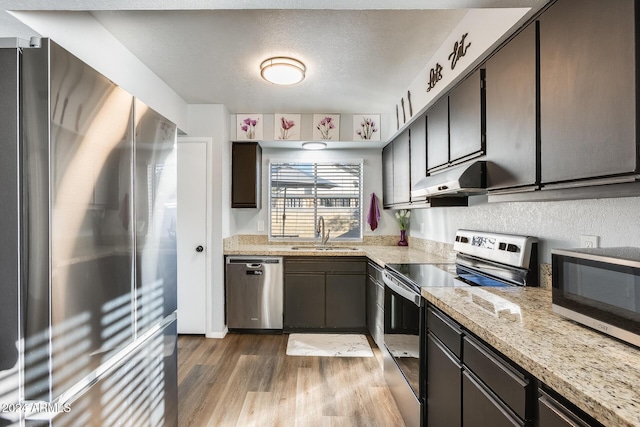 kitchen featuring appliances with stainless steel finishes, light wood-type flooring, light stone counters, a textured ceiling, and sink