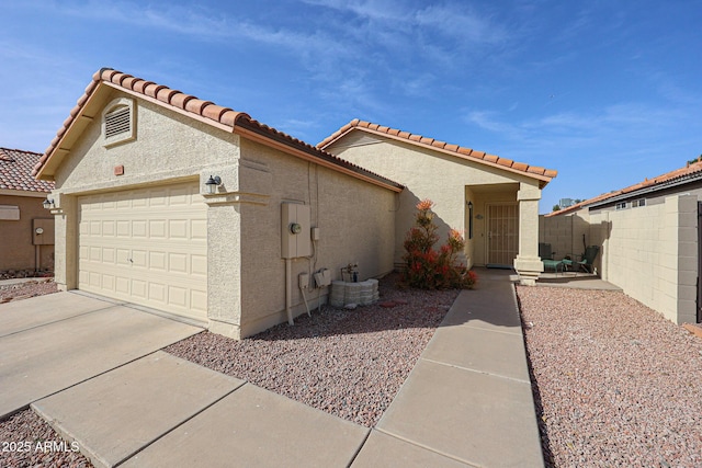 view of side of property featuring stucco siding, fence, a garage, driveway, and a tiled roof