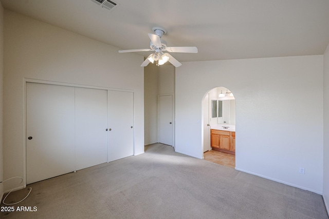 unfurnished bedroom featuring arched walkways, lofted ceiling, light carpet, visible vents, and a closet