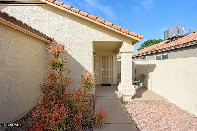 entrance to property with central AC, a tile roof, fence, and stucco siding