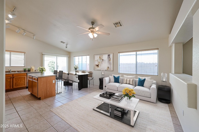 living area featuring vaulted ceiling, light tile patterned floors, visible vents, and a ceiling fan