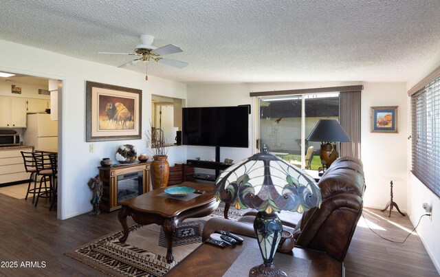 living area with a ceiling fan, a glass covered fireplace, wood-type flooring, and a textured ceiling