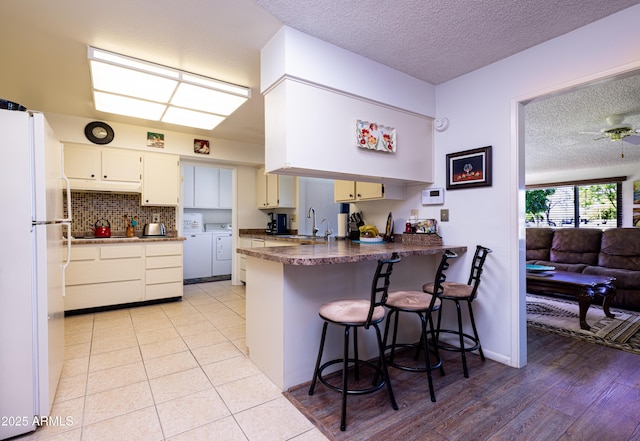 kitchen featuring washing machine and clothes dryer, a peninsula, freestanding refrigerator, a textured ceiling, and a sink