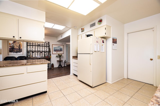 kitchen featuring light tile patterned flooring, white cabinets, and freestanding refrigerator