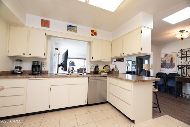 kitchen featuring light tile patterned floors, stainless steel dishwasher, a sink, a peninsula, and a kitchen bar