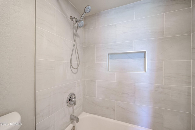 bathroom with tiled shower / bath combo and toilet