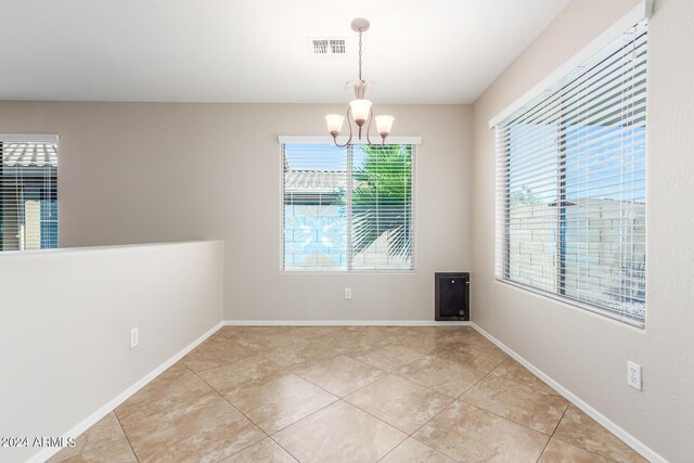 tiled empty room featuring an inviting chandelier and a wealth of natural light