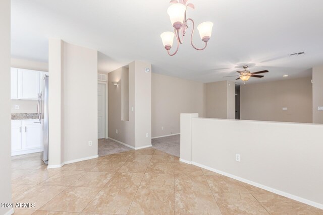 tiled empty room with ceiling fan with notable chandelier