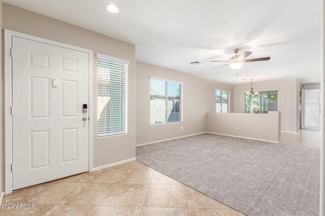 foyer featuring ceiling fan with notable chandelier, light colored carpet, and plenty of natural light