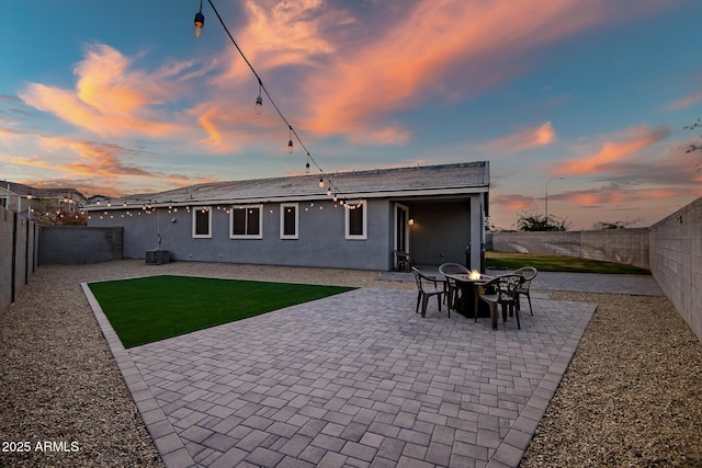 back house at dusk featuring an outdoor fire pit, a yard, central AC unit, and a patio area