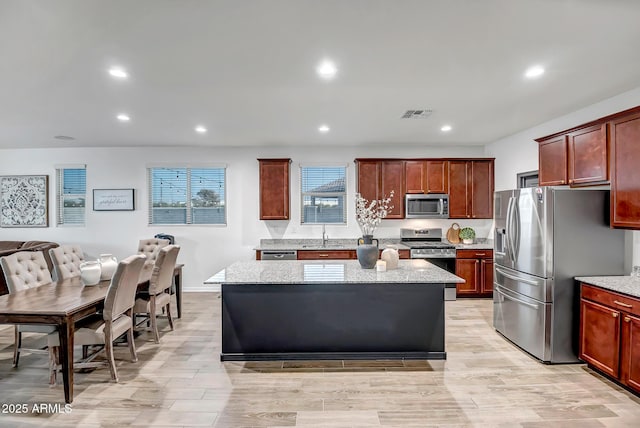 kitchen with light stone counters, appliances with stainless steel finishes, a center island, and light hardwood / wood-style floors