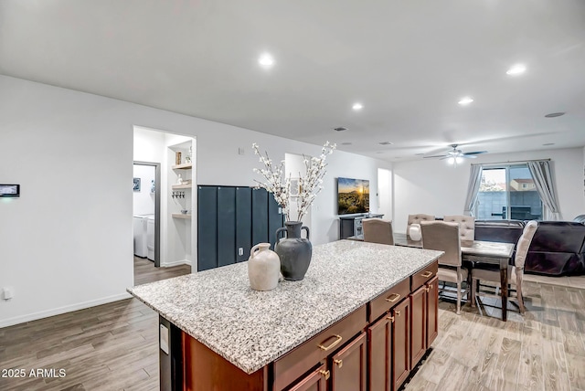 kitchen with ceiling fan, light stone countertops, a center island, and light wood-type flooring