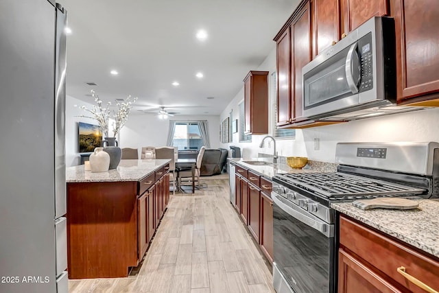 kitchen with sink, light stone counters, appliances with stainless steel finishes, ceiling fan, and light hardwood / wood-style floors