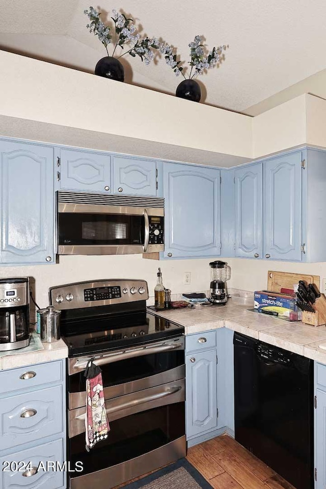 kitchen featuring light hardwood / wood-style floors, blue cabinets, stainless steel appliances, and vaulted ceiling