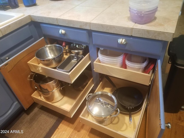 interior details featuring tile countertops, hardwood / wood-style flooring, and blue cabinets