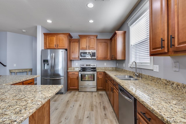 kitchen featuring appliances with stainless steel finishes, sink, light stone counters, and light wood-type flooring