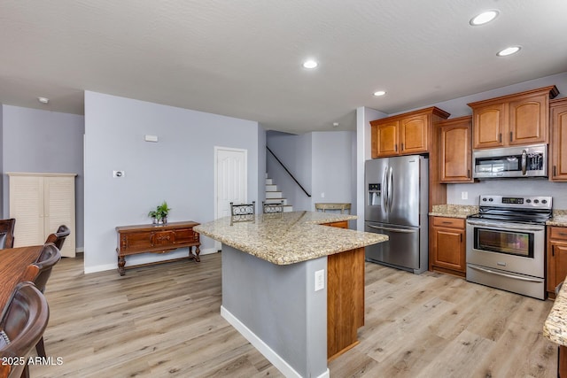 kitchen featuring stainless steel appliances, light stone countertops, light hardwood / wood-style floors, a textured ceiling, and a kitchen island