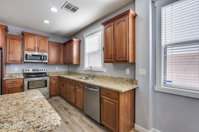 kitchen featuring sink, light hardwood / wood-style flooring, light stone countertops, and appliances with stainless steel finishes