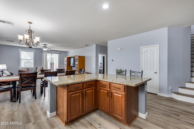 kitchen featuring pendant lighting, a center island, light stone counters, and light hardwood / wood-style flooring