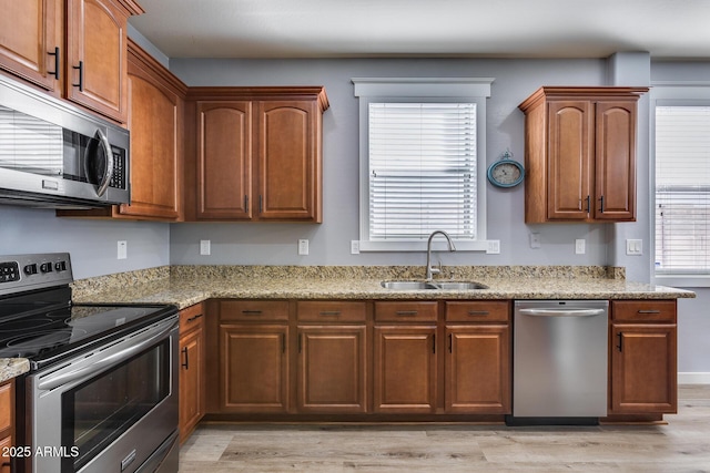 kitchen with stainless steel appliances, light stone countertops, sink, and light wood-type flooring