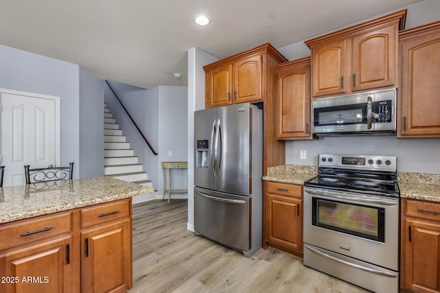 kitchen featuring light stone counters, stainless steel appliances, and light wood-type flooring