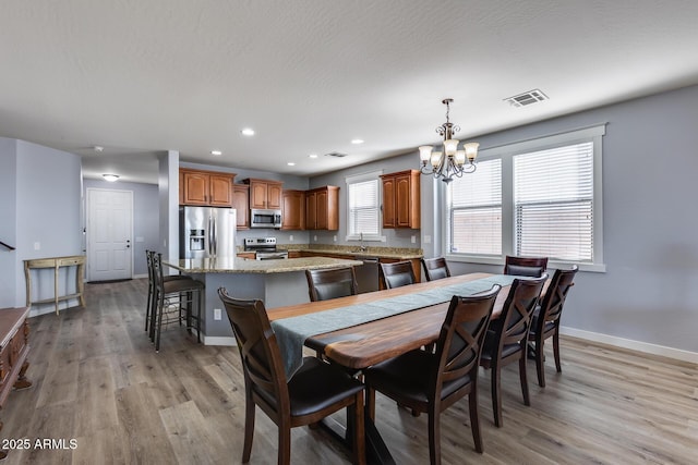 dining space with sink, an inviting chandelier, and light wood-type flooring