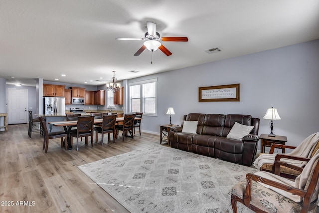 living room featuring ceiling fan with notable chandelier and light hardwood / wood-style flooring