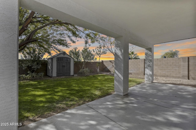 yard at dusk featuring a storage unit and a patio area