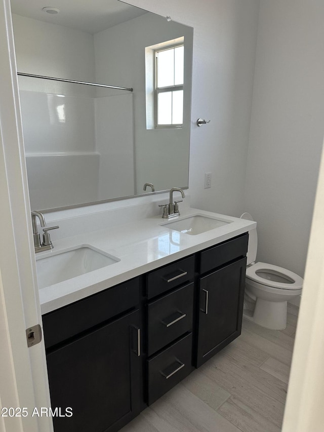 full bath featuring wood finished floors, a sink, toilet, and double vanity