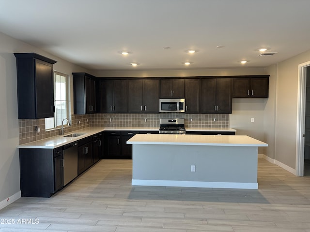 kitchen with stainless steel appliances, a sink, light wood-style floors, light countertops, and a center island